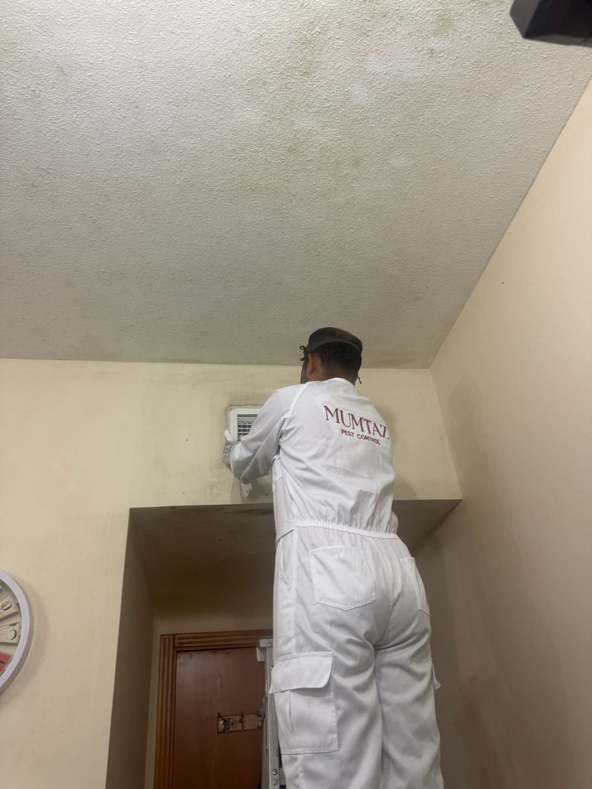 Technician on a stepladder examining an AC supply grille and the stained wall around it